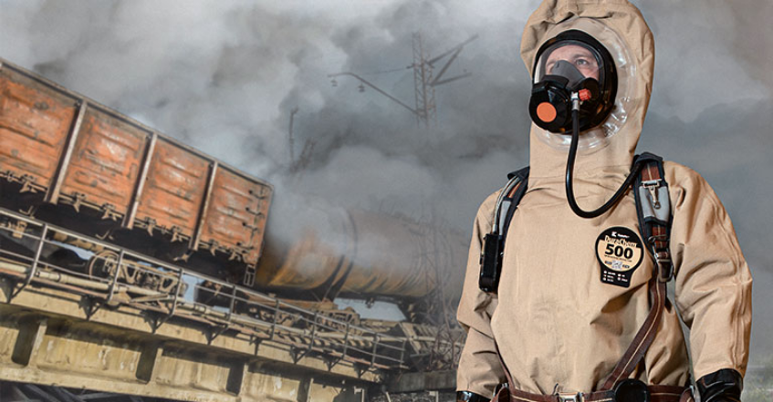 Worker in a tan Kappler DuraChem 500 suit and respirator at a smoking train derailment