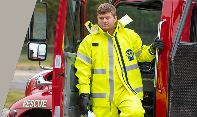Responder in a hi-vis yellow Kappler DuraChem 200 suit stepping down from a rescue truck