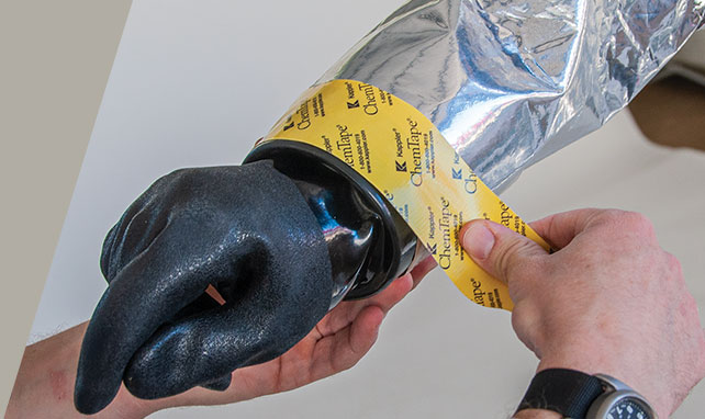 Hands sealing a suit glove to the sleeve cuff with yellow Kappler ChemTape
