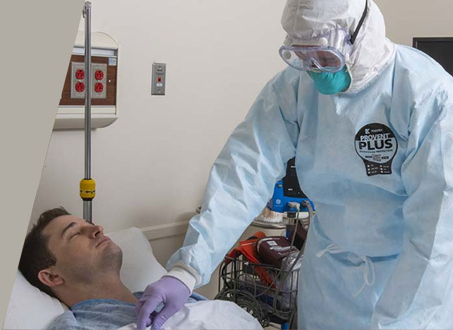 Caregiver in a Kappler ProVent Plus gown and hooded respirator attending a patient in a hospital bed