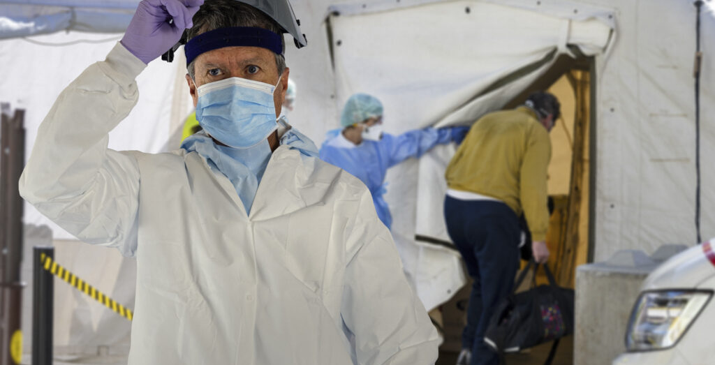 Worker in a white Kappler protective coverall and face shield at an outdoor medical screening tent