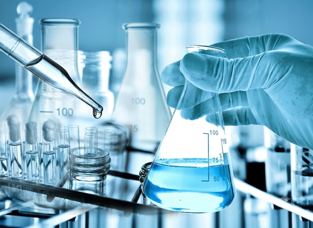 Gloved hand holding a blue-liquid flask among lab beakers and test tubes